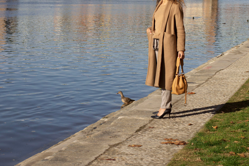 Model carring a leather bucket bag in tan color near a lake